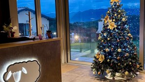Un área de recepción con un gran árbol de Navidad, una lámpara con forma de oveja y vistas a un paisaje urbano al atardecer.
