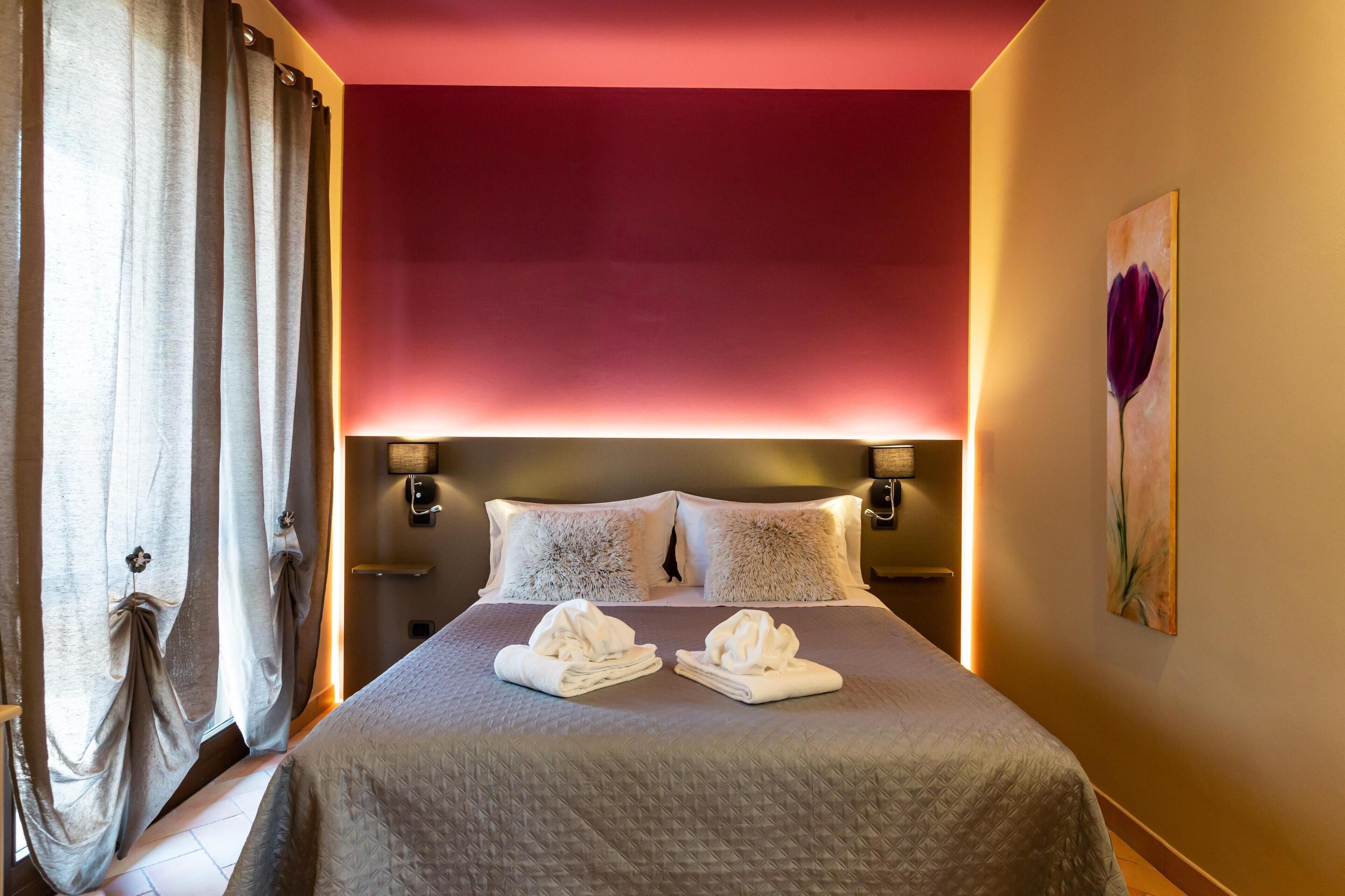 Camera d'albergo con un letto, due cuscini, una testiera, un quadro e una finestra con tende.