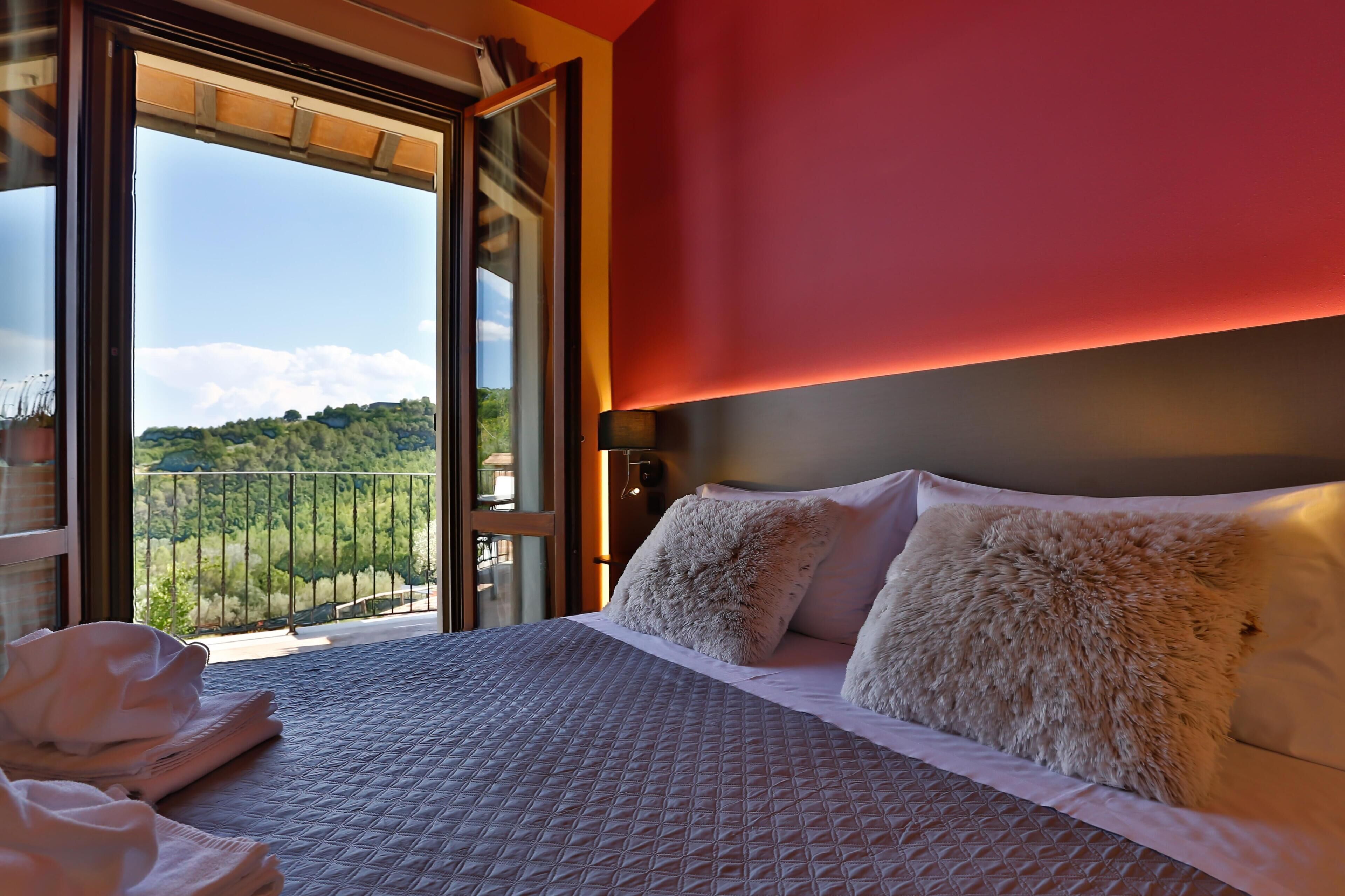 Habitación de hotel con cama, almohadas, una ventana y vistas a un paisaje verde.