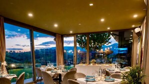 Un restaurante con mesas dispuestas para comer, grandes ventanales que ofrecen vistas al exterior e iluminación empotrada en el techo.