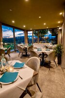 Un restaurante con mesas dispuestas para comer, grandes ventanales que ofrecen vistas al exterior e iluminación empotrada en el techo.