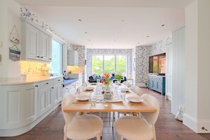 Una cocina amplia con comedor, armarios blancos y un ventanal que proporciona luz natural.