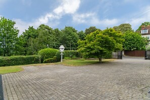 A paved driveway leading to a house with a white fence and a small white structure.