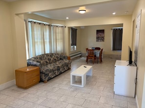 Ein Wohnzimmer mit Sofa, Couchtisch, TV-Schrank, Esstisch mit Stühlen und einer kleinen Kommode.