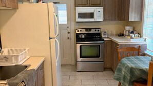 Una cocina con armarios de madera, un refrigerador blanco, un microondas, un horno, un lavamanos y una mesa de comedor con mantel verde.