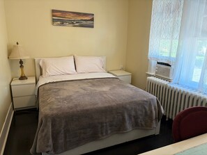 Ein Schlafzimmer mit einem Bett, einem Nachttisch, einer Lampe, einem Heizkörper und einem Fenster mit Vorhängen.