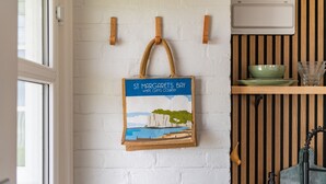 A kitchen with a white brick wall, wooden shelves, and a hanging bag with a coastal scene.