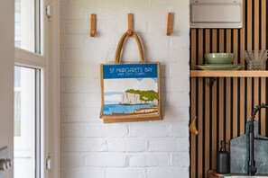 A kitchen with a white brick wall, wooden shelves, and a hanging bag with a coastal scene.