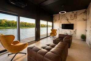 Ein modernes Wohnzimmer mit großen Fenstern, einem Flachbildfernseher und Ledersofas.