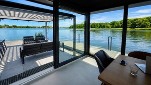 A modern interior with a large glass window overlooking a lake, a wooden table, and a seating area with a view.