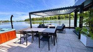 An outdoor patio with a table and chairs, a hot tub, and a view of a lake.