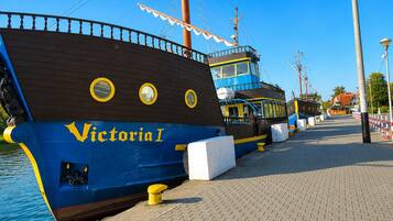 Un navire amarré, baptisé « Victoria I », avec une coque bleue et des éléments de couleur jaune, est accosté à un quai, sous un ciel dégagé.