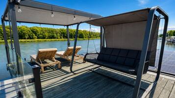 A deck with a swing chair and two lounge chairs, overlooking a body of water.
