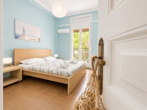 A bedroom with a wooden bed, a nightstand, a wall-mounted air conditioner, and a view of greenery outside. - The Acropolis Neighbourhood Experience Apt by ΜΡS (Athina)