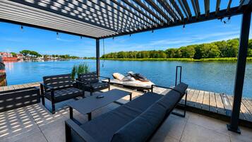 Un espace extérieur abrité, aménagé avec des sièges, d’où l’on peut admirer un lac, un jet ski et un bateau amarré au loin.