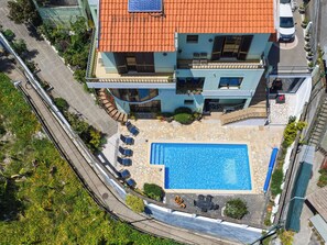 Ein mehrstöckiges Gebäude mit Solaranlage auf dem Dach, einem Schwimmbad und einer überdachten Außenbereich-Sitzgelegenheit.