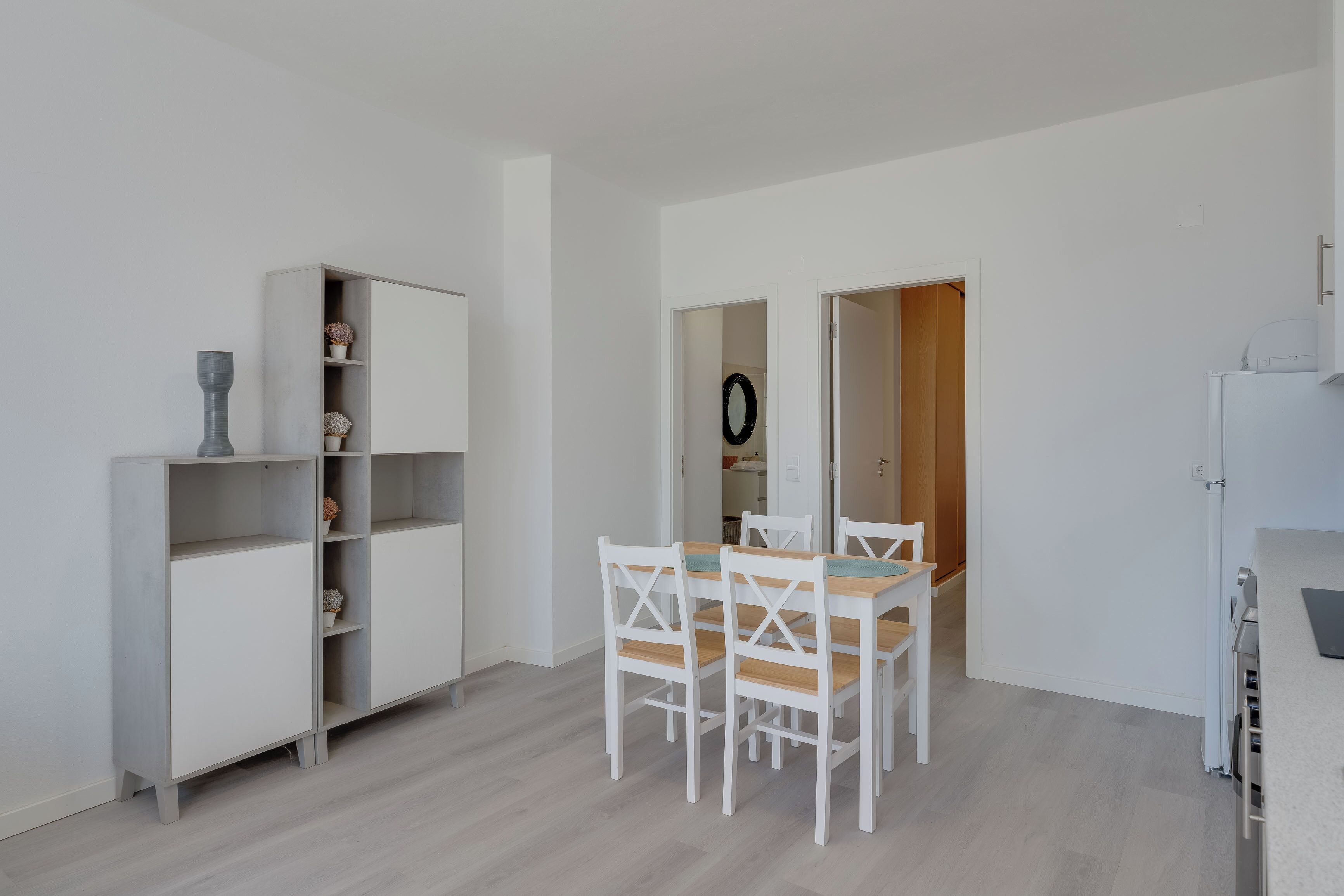 A modern kitchen with white cabinetry, a dining table with chairs, and a refrigerator.