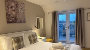 A hotel room with a bed, a large window with curtains, a balcony, and a wall-mounted artwork. - Sheraton Apartments (Fort William)