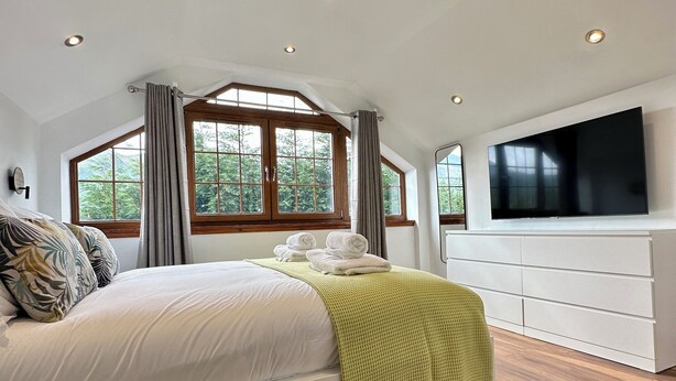 A bedroom with a large bed, wooden flooring, a TV, and a window with curtains. - Sheraton Apartments (Fort William)