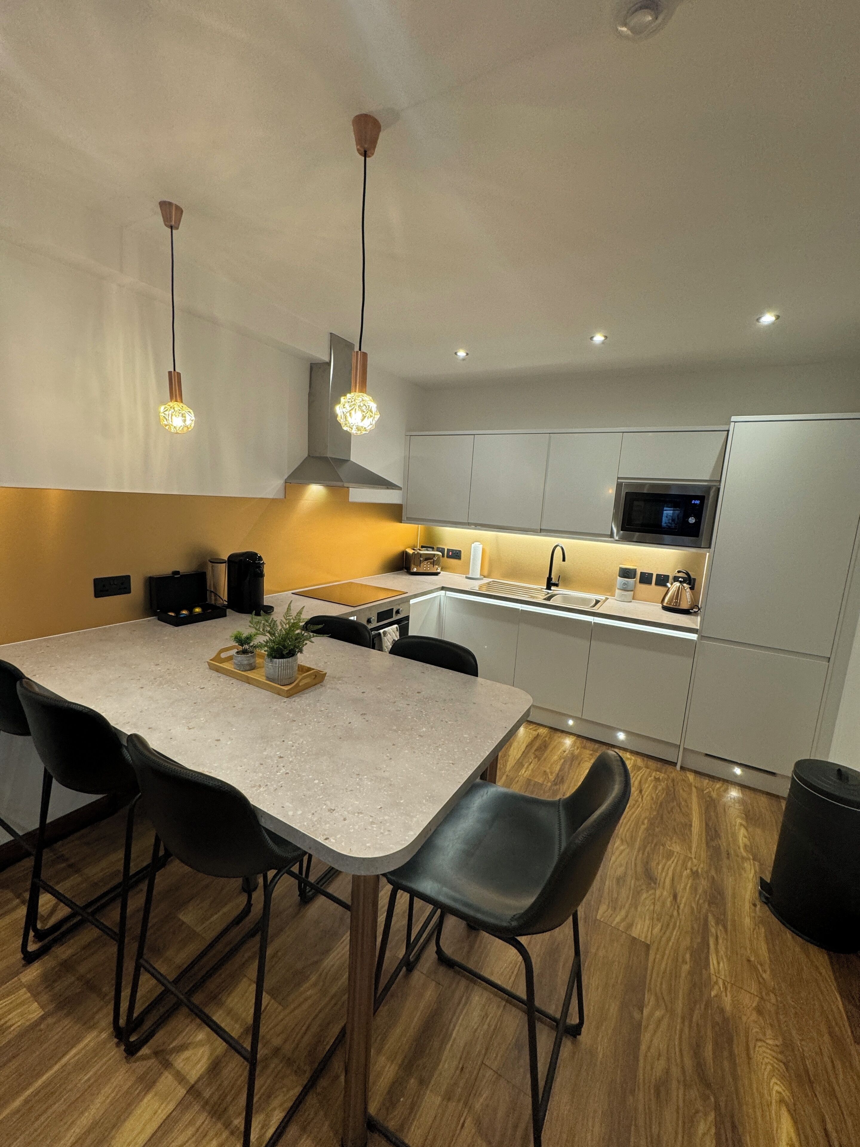 Una cocina moderna con una isla central, iluminación colgante y electrodomésticos de acero inoxidable.