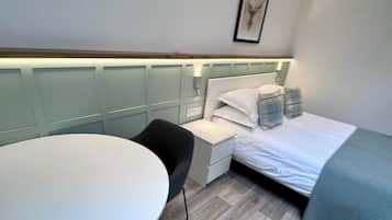 Een kleine hotelkamer met een bed, nachtkastje, stoel en een bureau met een stoel.