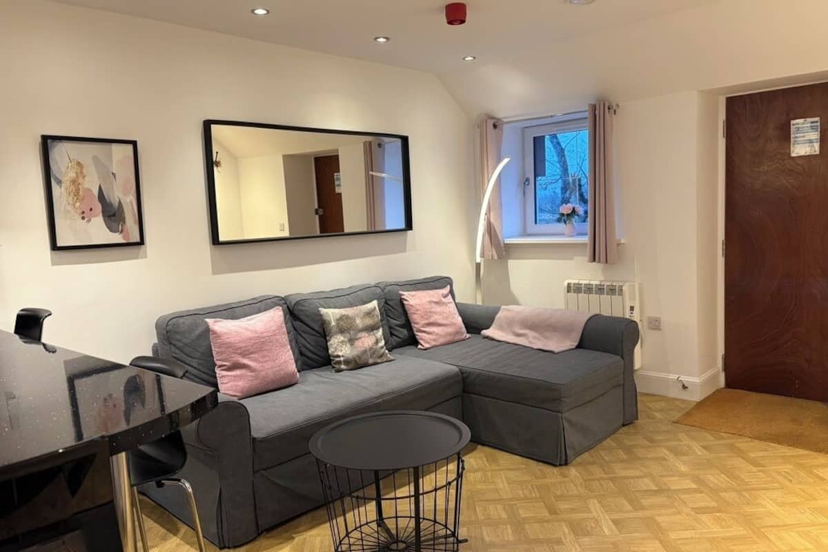 A modern living room with a sectional sofa, a round coffee table, a dining table, a large mirror, and a window with curtains.