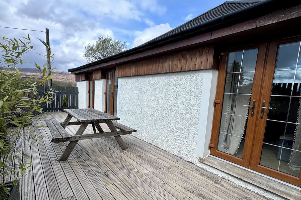 A wooden deck with a picnic table, a building with large windows, and a view of the sky.