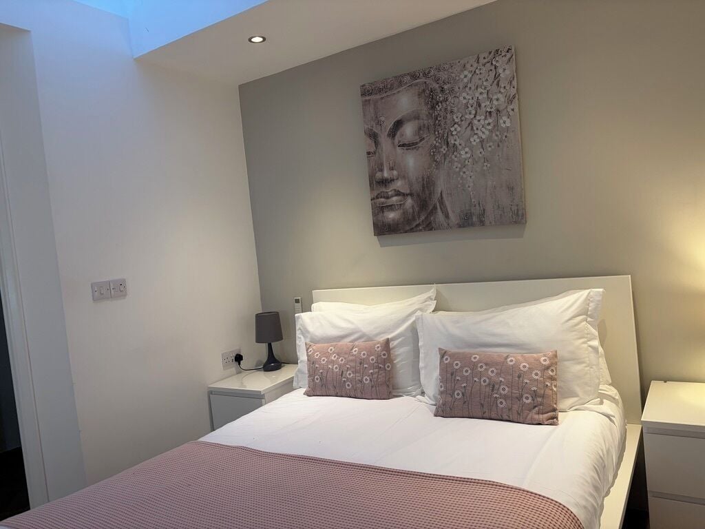 A bedroom with a bed, two bedside tables, a wall-mounted artwork, and a ceiling light.