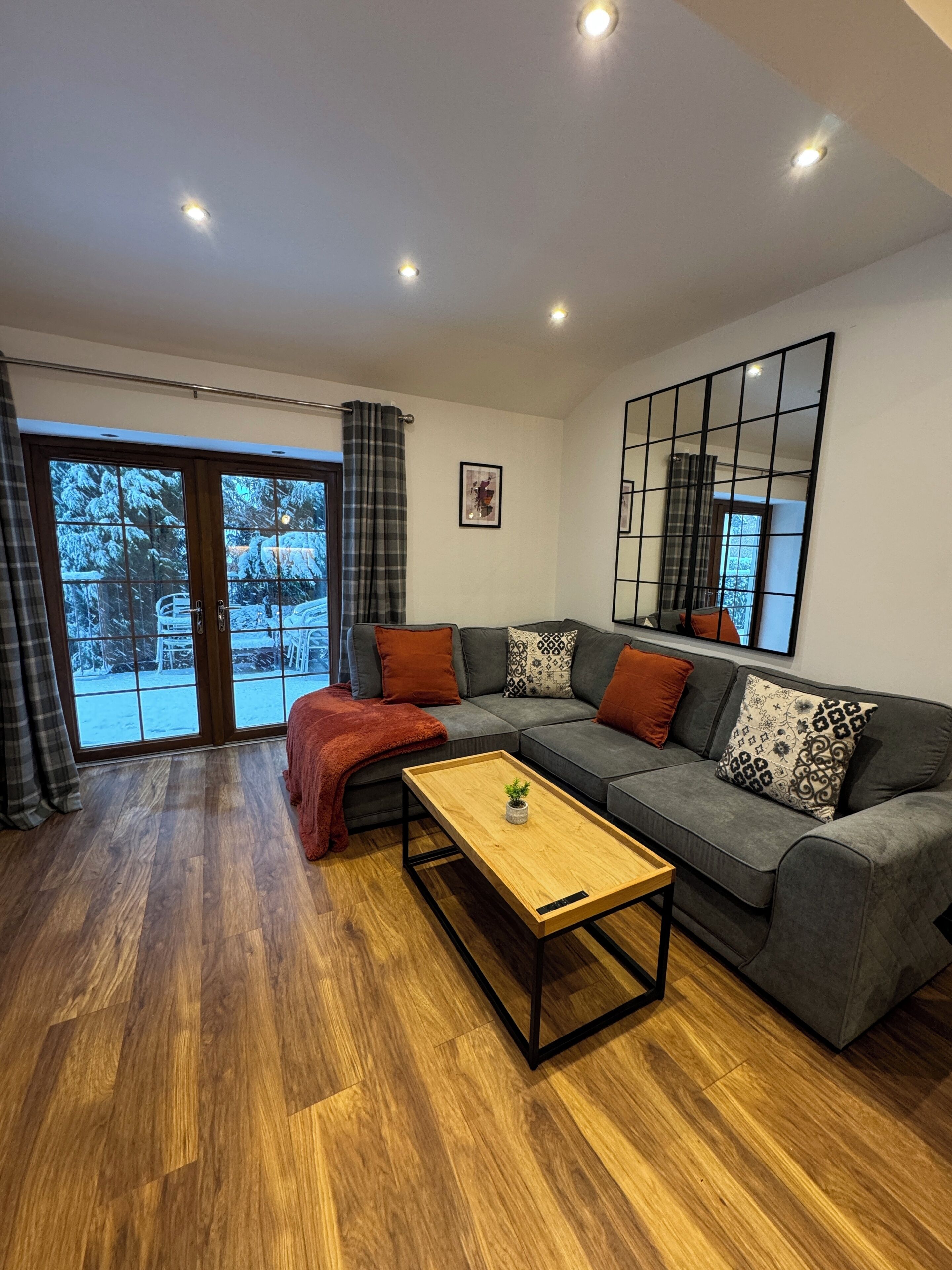 Una sala de estar moderna con un sofá gris, una mesa de centro de madera y un ventanal con vistas a un paisaje nevado.