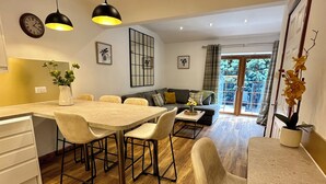 A modern kitchen with a dining area, wooden flooring, pendant lights, and a view through a glass door. - Sheraton Apartments (Fort William)