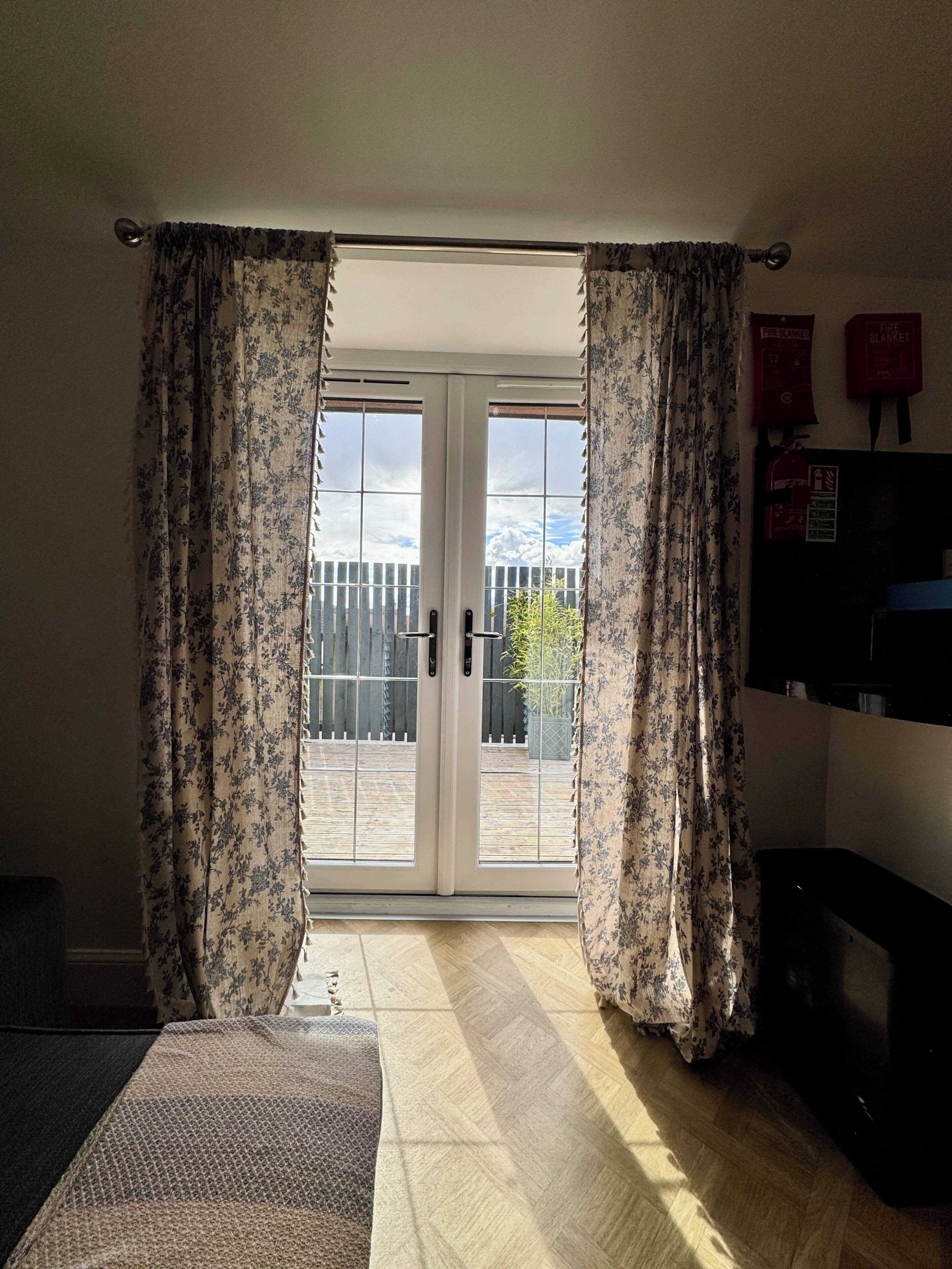 Una habitación con puerta de vidrio corredera que da a un espacio exterior, una cama, una mesita y un aviso de seguridad contra incendios en la pared.