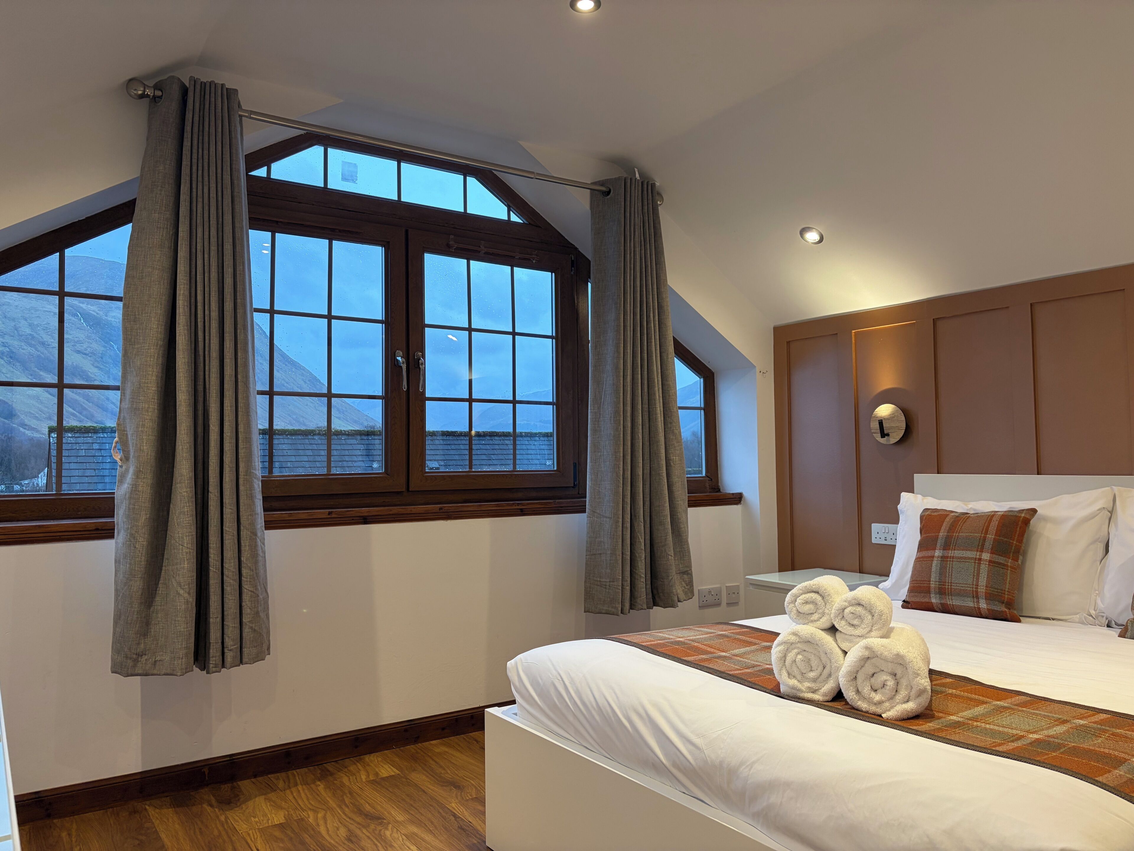 Een slaapkamer met een groot raam, een bed met witte lakens en een hoofdeinde met een klok.