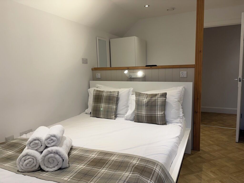 A hotel room with a bed, pillows, a bedside lamp, and a stack of towels.