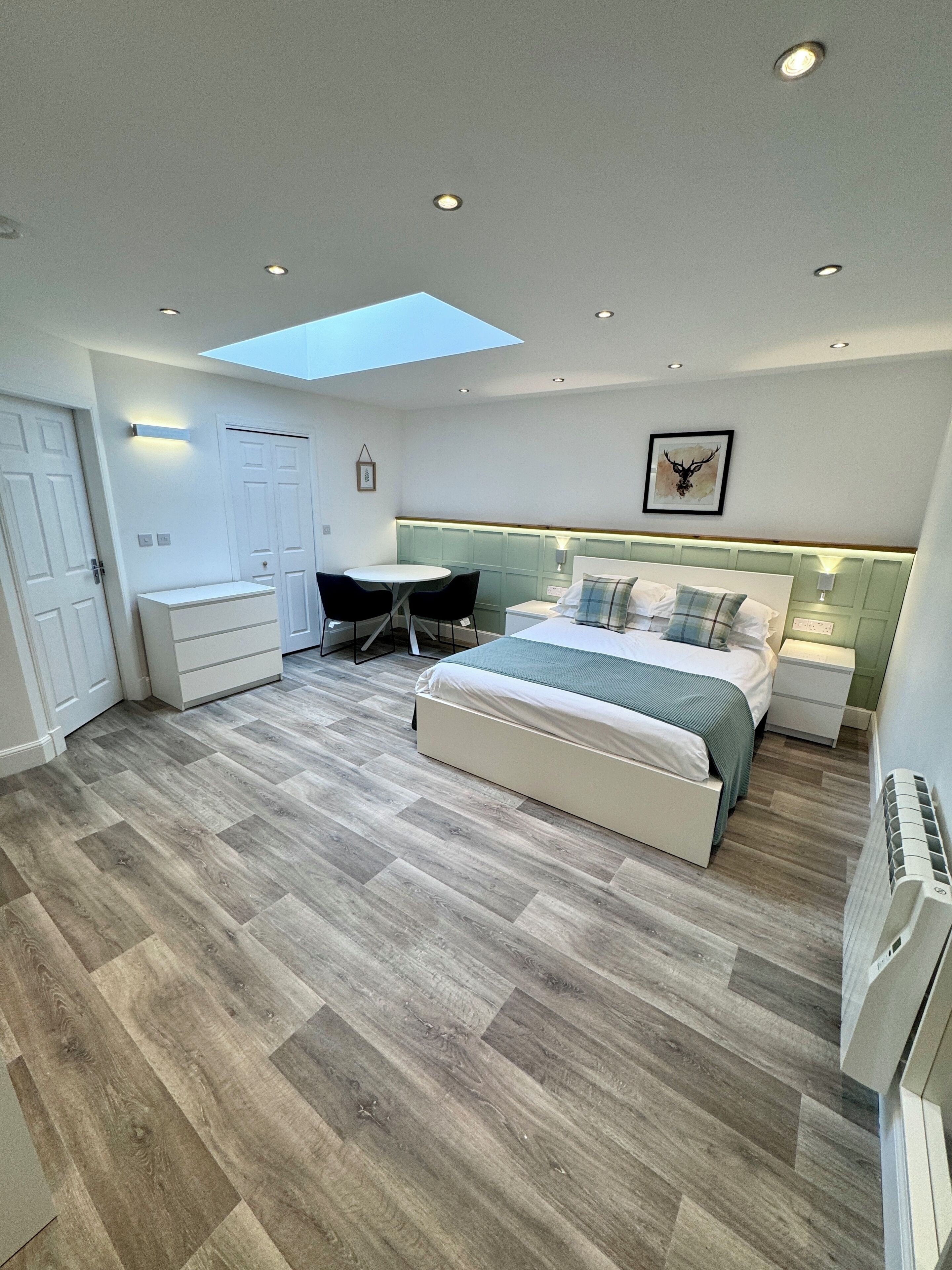 A modern bedroom with a skylight, a bed, bedside tables, a desk, and a chair.