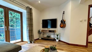 A modern living room with a flat-screen TV, a guitar, and a dining table with a tray of plants. - Sheraton Apartments (Fort William)
