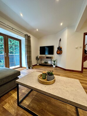 Uma sala de estar moderna com uma televisão de tela plana, um violão e uma mesa de jantar com uma bandeja de plantas.