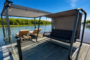 A deck with a swing chair and two lounge chairs, overlooking a body of water.