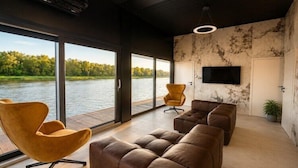 Een moderne woonkamer met grote ramen, een flatscreen televisie en leren banken.