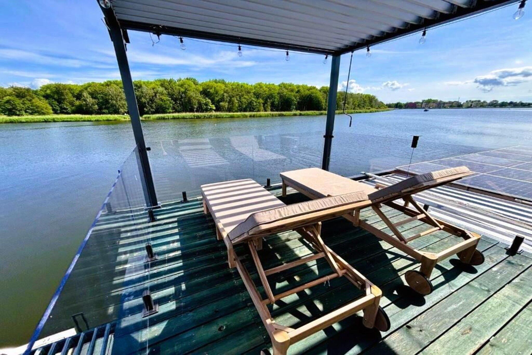 Um deck coberto com cadeiras de descanso e uma mesa, com vista para um corpo d'água calmo.