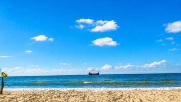 Une plage avec un ciel dégagé, une mer calme et un bateau à l’horizon.