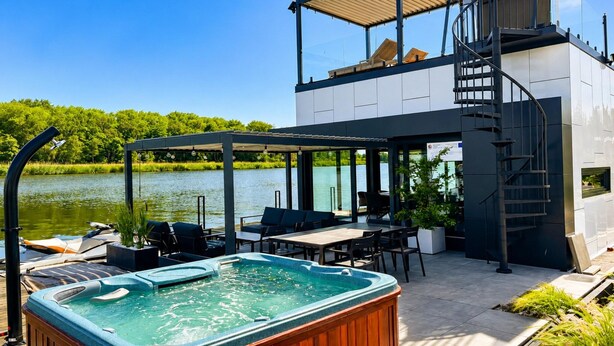A modern outdoor pool area with a hot tub, seating, and a view of a lake.