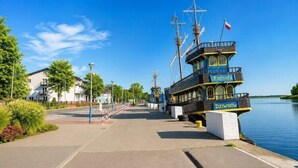 A waterfront promenade with a tall, narrow building labeled 'Kostrz' and 'Dziwnów' docked at the pier. - Charming Dziwnów House with a jacuzzi (Dziwnów)
