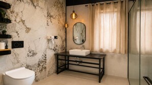 A bathroom with a white toilet, a marble wall, a black vanity with a mirror, and a shower area.