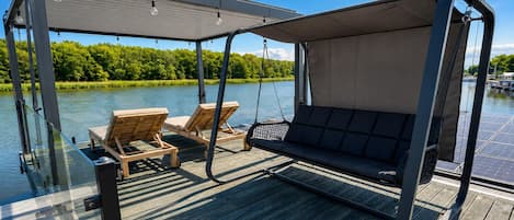 A deck with a swing chair and two lounge chairs, overlooking a body of water.