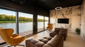 Ein modernes Wohnzimmer mit großen Fenstern, einem Flachbildfernseher und Ledersofas.