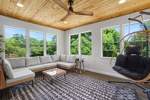Una habitación con techo de madera, ventanas amplias, sofá modular, una silla colgante y alfombra estampada.