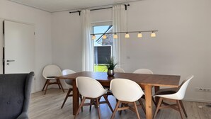 En matplats med ett träbord, vita stolar, en grå soffa och en taklampa.