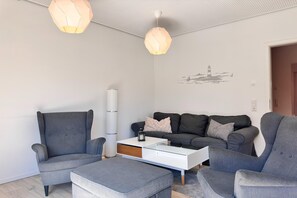 Ein modernes Wohnzimmer mit grauen Polstermöbeln, einem weißen Couchtisch mit Stauraum und zwei Pendelleuchten.