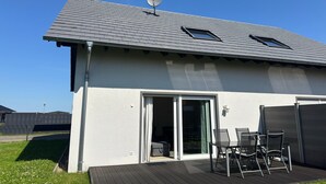 Ett modernt hus med en satellitparabol, en skjutdörr i glas och en terrass med stolar.