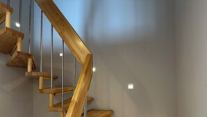 Een houten trap met metalen leuningen, leidend naar een plateau met een lichtschakelaar.